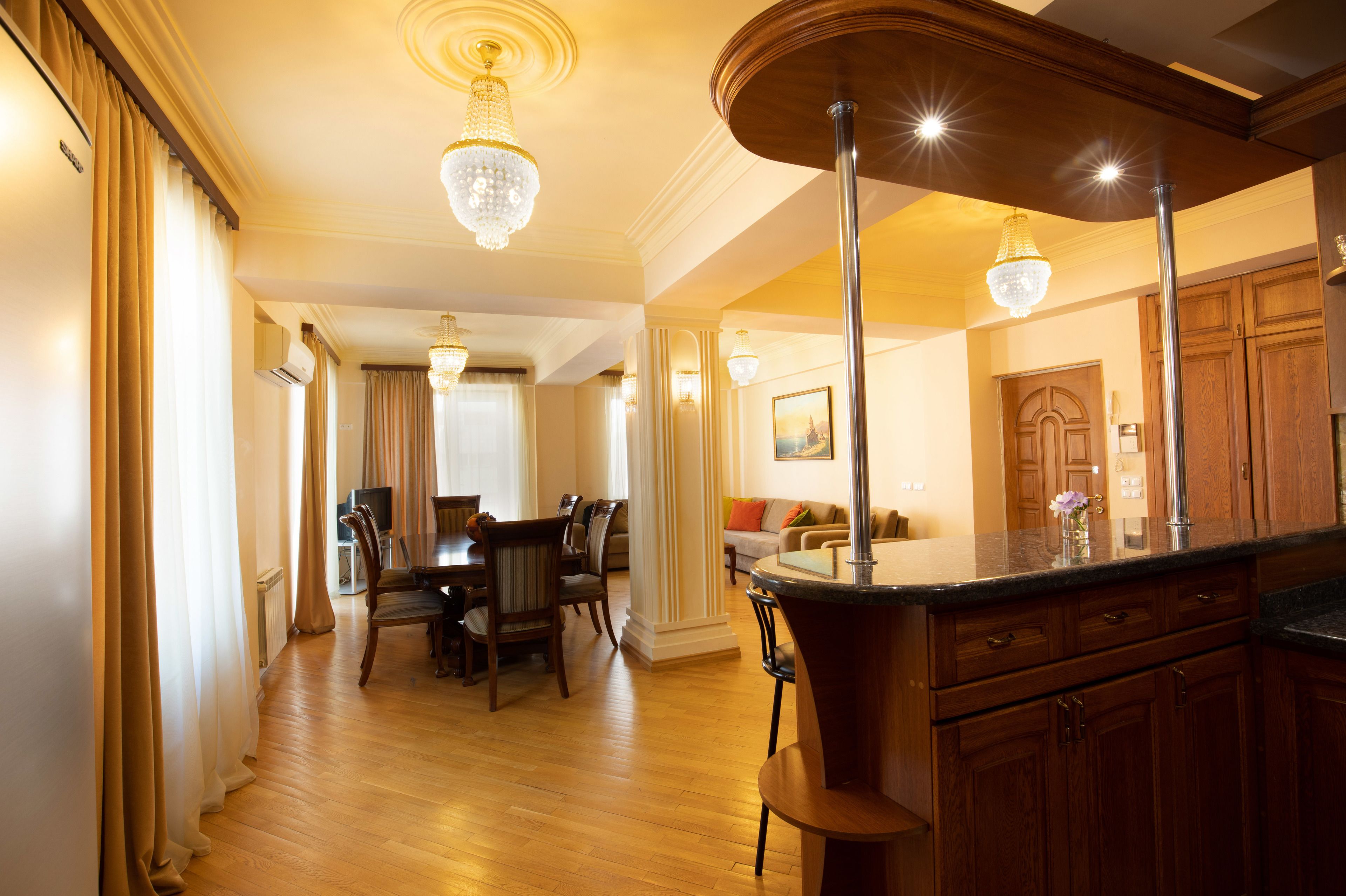 Un vaste espace dédié à la salle à manger, avec une table et des chaises en bois, un lustre, et une vue sur le salon, où se trouvent un canapé et un téléviseur.