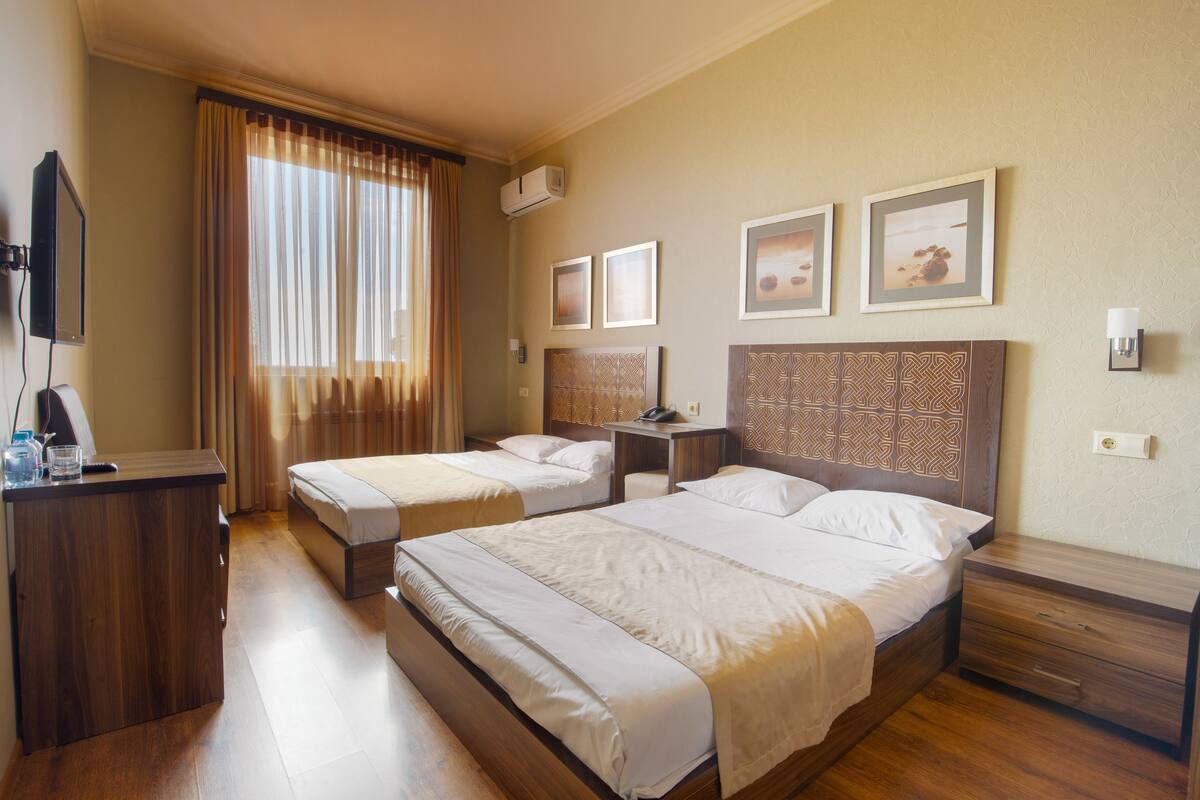 A hotel room with two beds, a desk, a TV, and a window with curtains.