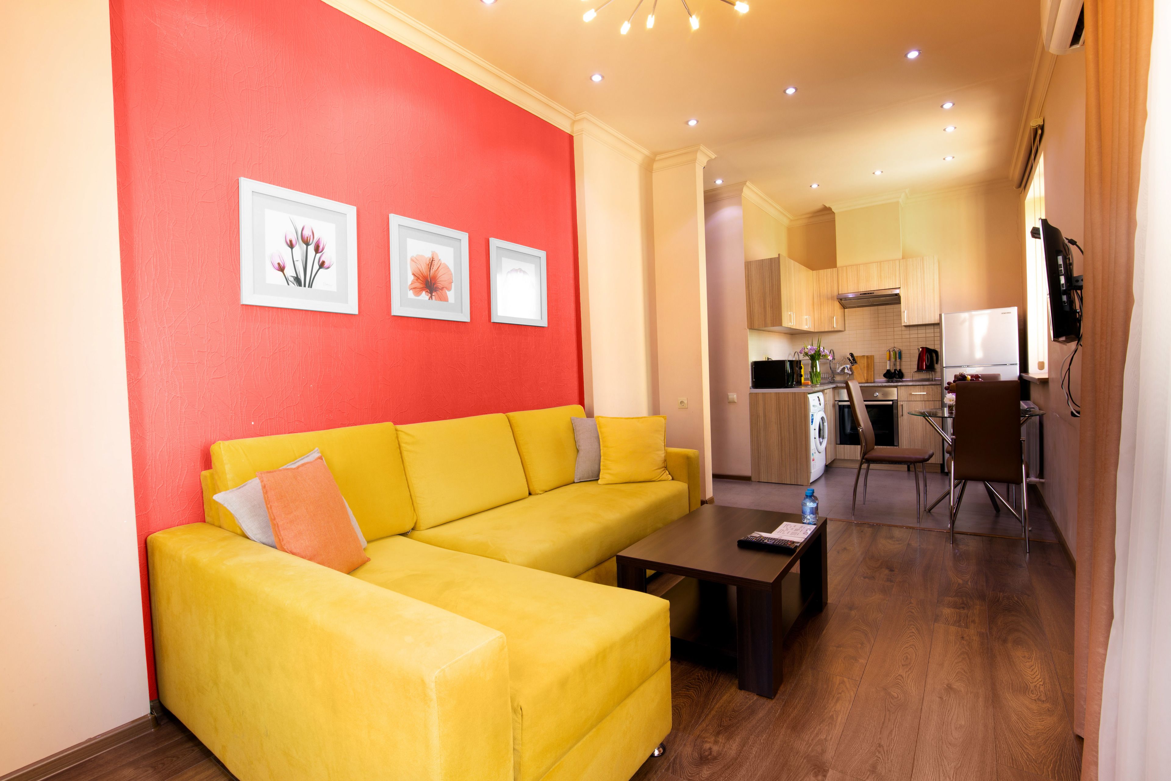 A bright yellow sofa with a coffee table in a modern living room with a red accent wall and framed artwork.
