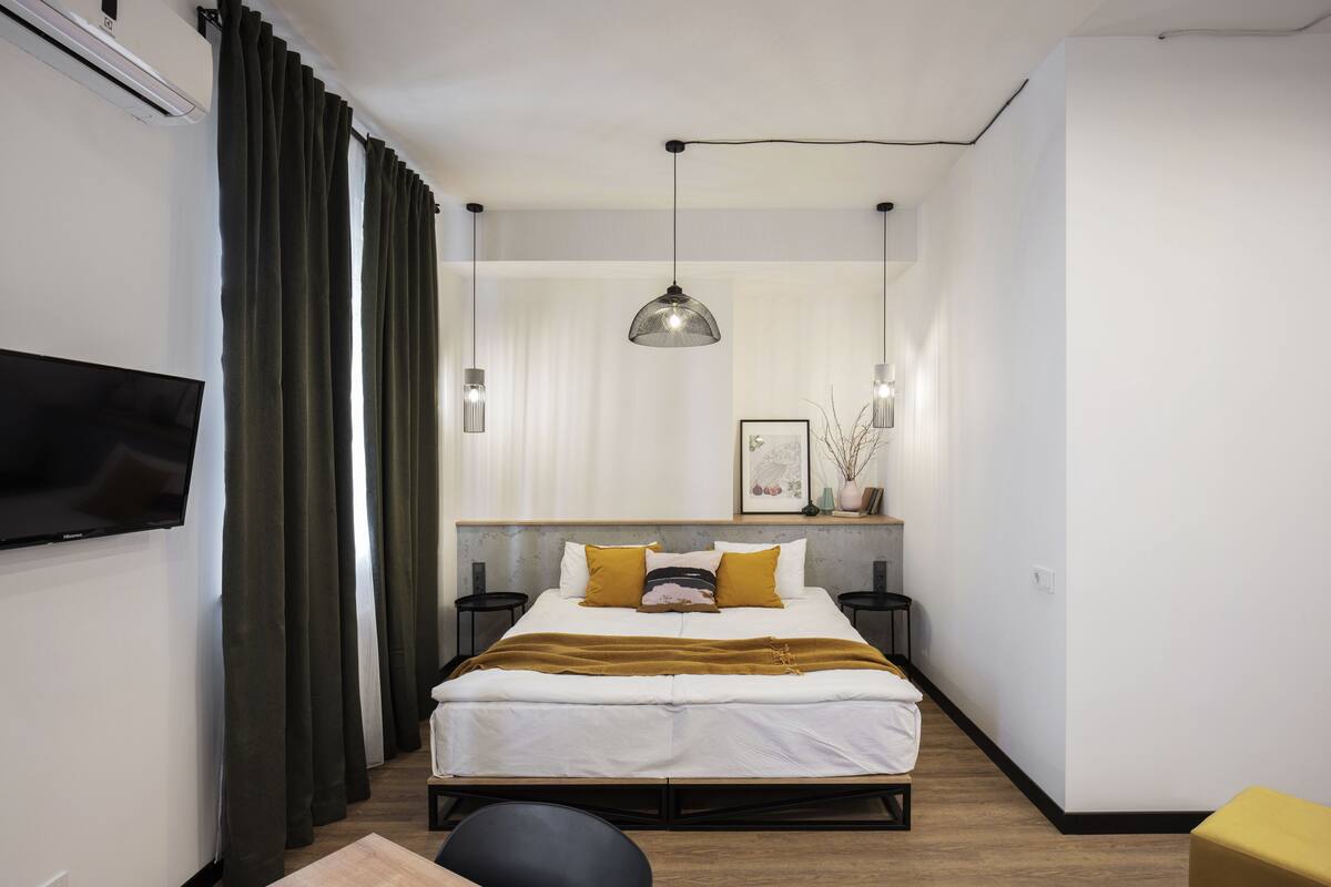 A modern hotel room with a bed, a TV, a desk, and a chair.