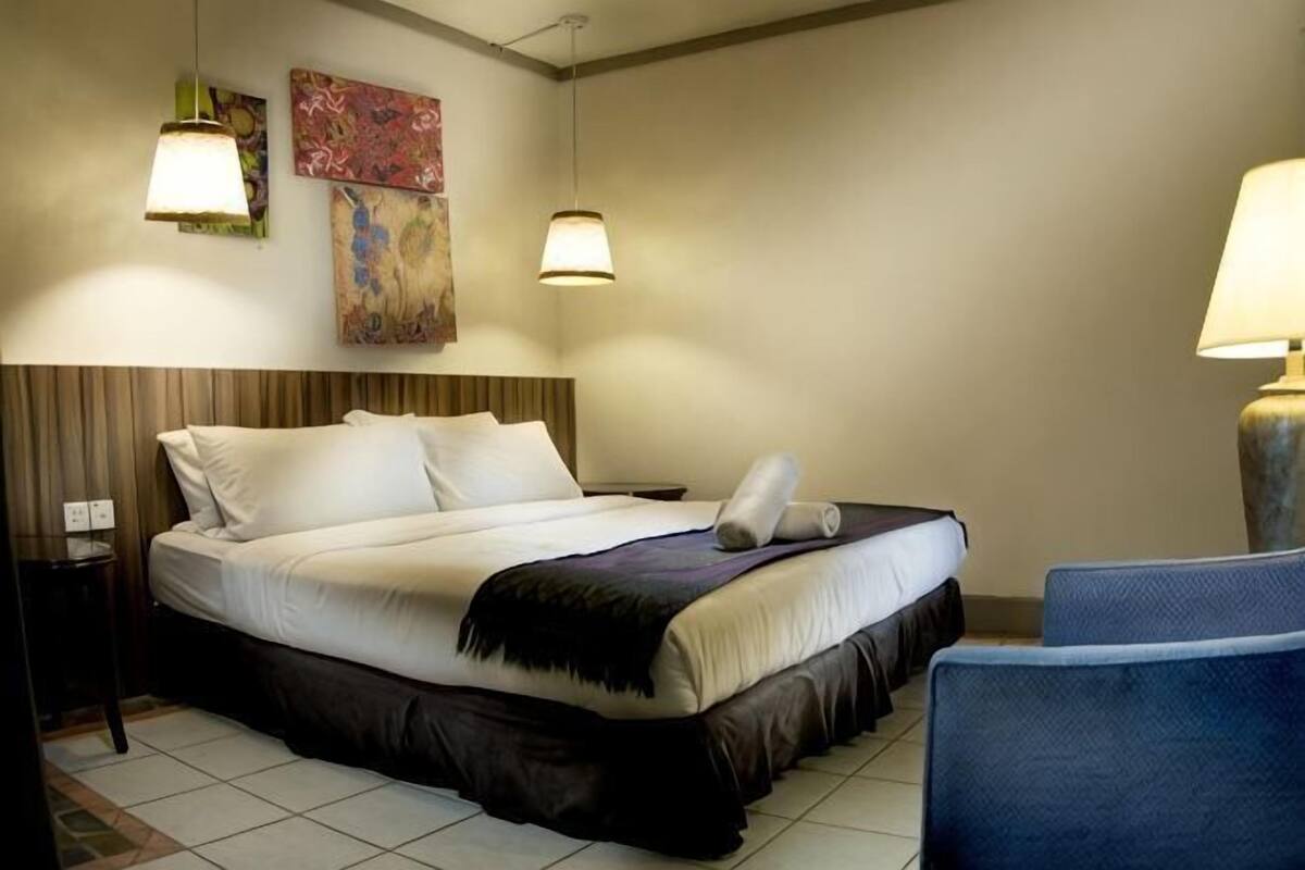 Ein Hotelzimmer mit Bett, Nachttischen, einem Sessel und einem Bild an der Wand.