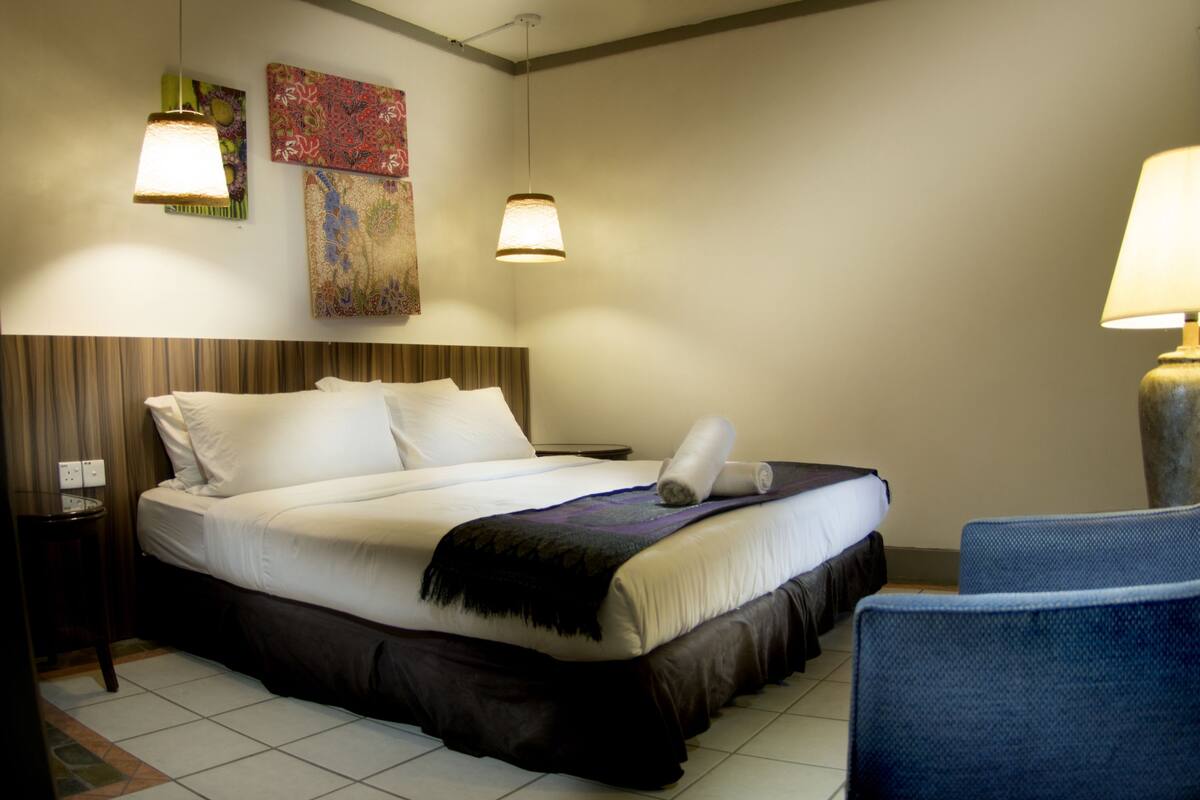 Ein Hotelzimmer mit einem Bett, zwei Nachttischlampen, einem Sessel und einem Kunstwerk an der Wand.