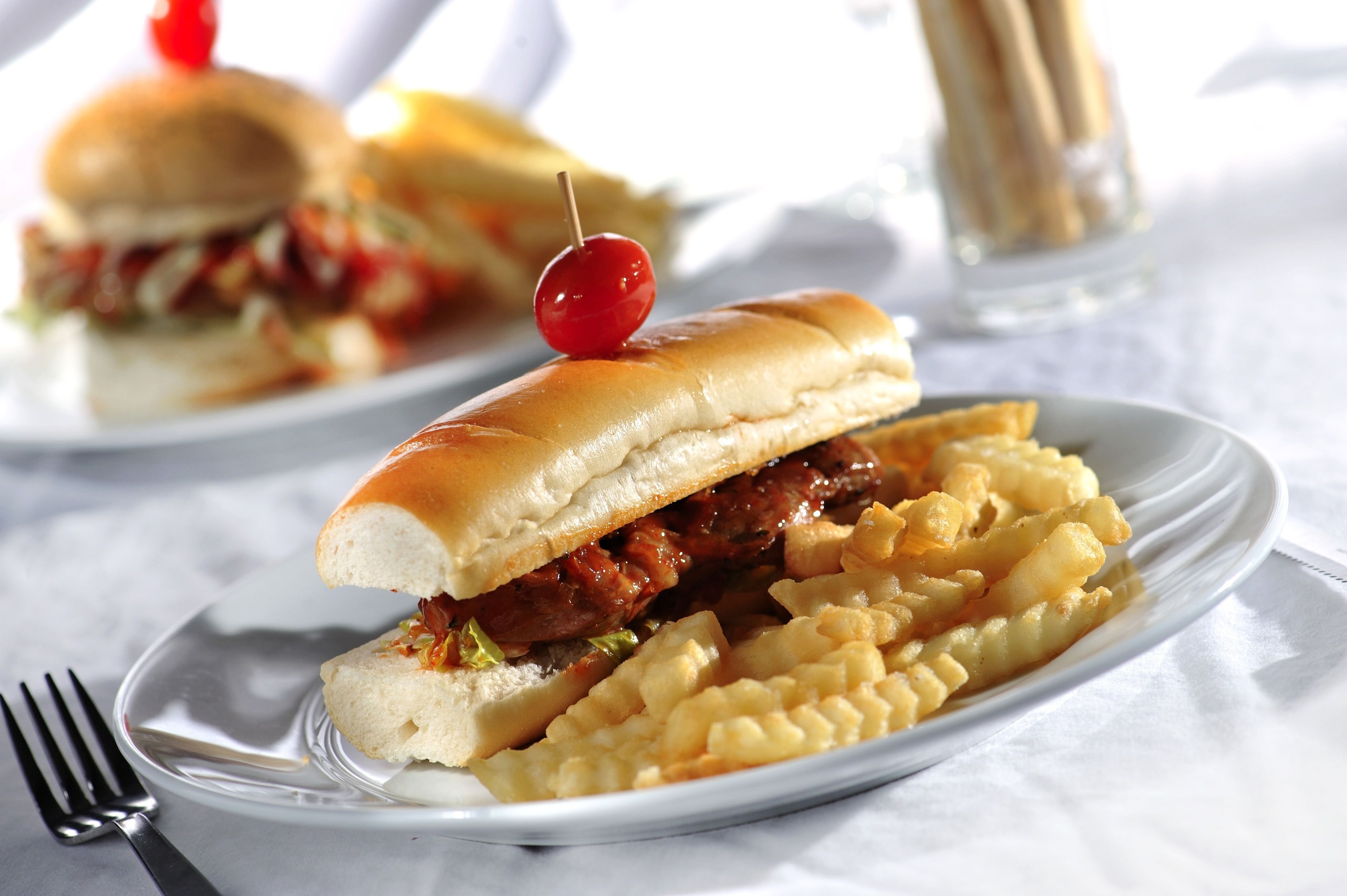 Un sándwich con cereza encima, acompañado de papas fritas en un plato blanco.