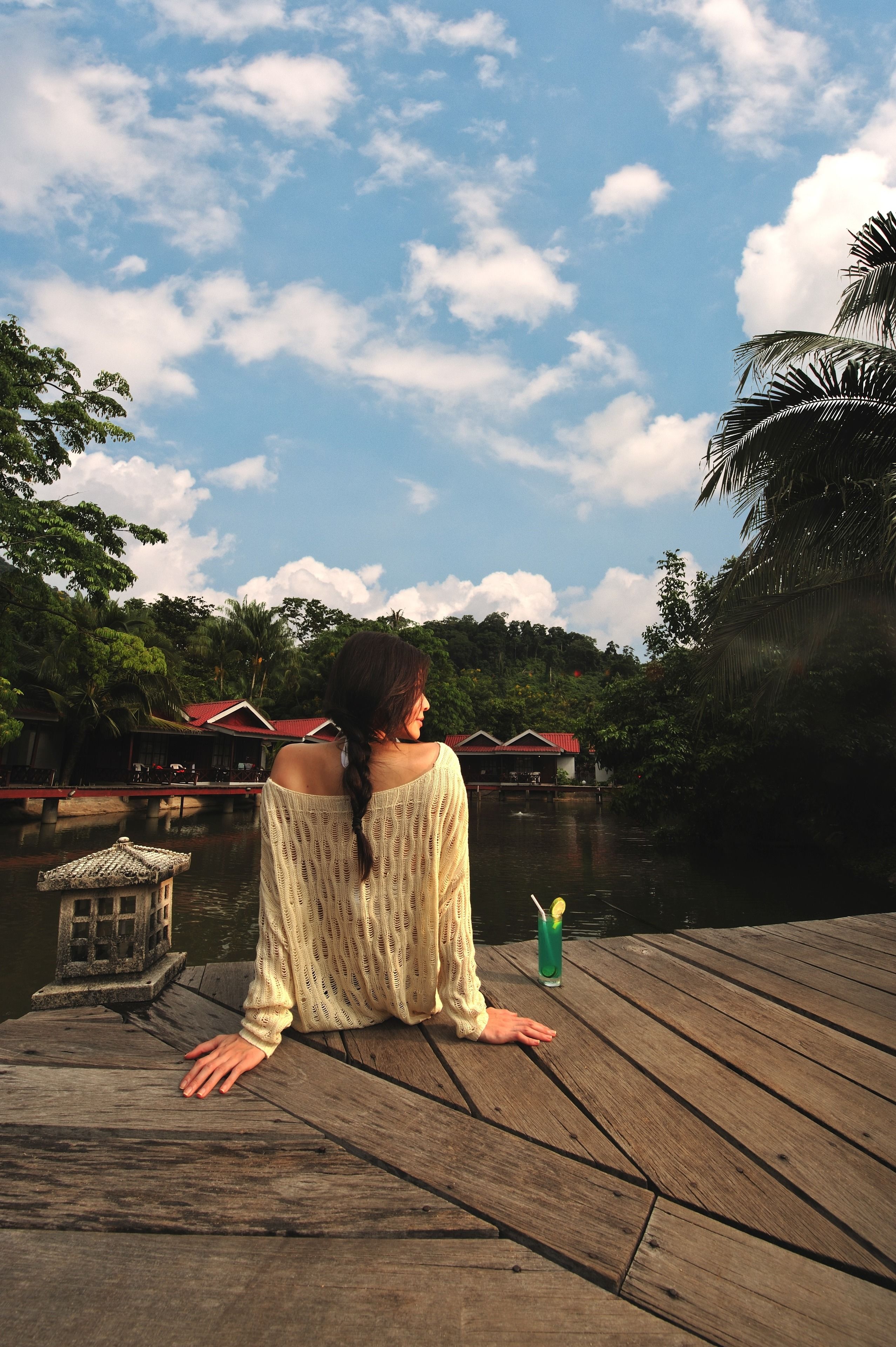 A person sitting on a wooden dock overlooking a body of water with houses in the background.