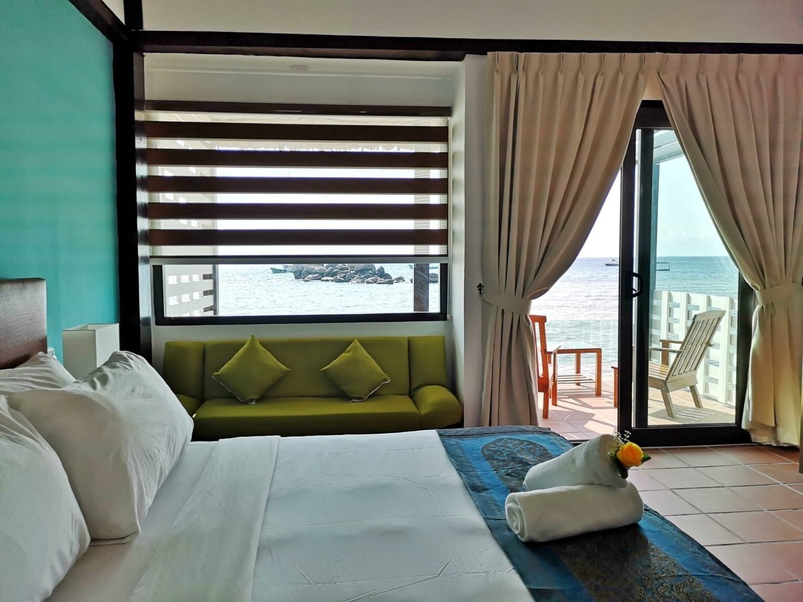 A hotel room with a bed, a green sofa, a view of the sea, and a balcony with chairs.