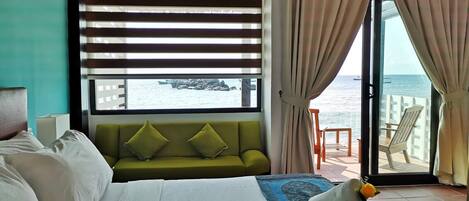 A hotel room with a bed, a green sofa, a view of the sea, and a balcony with chairs.