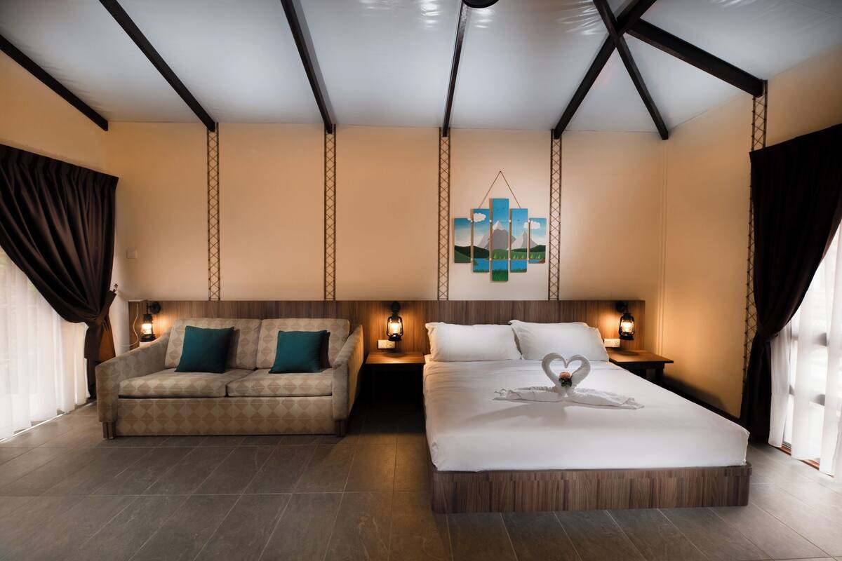 Ein Hotelzimmer mit einem großen Bett, einer Couch, zwei Nachttischen mit Lampen, einem Wandbild und einer Holzbalkendecke.
