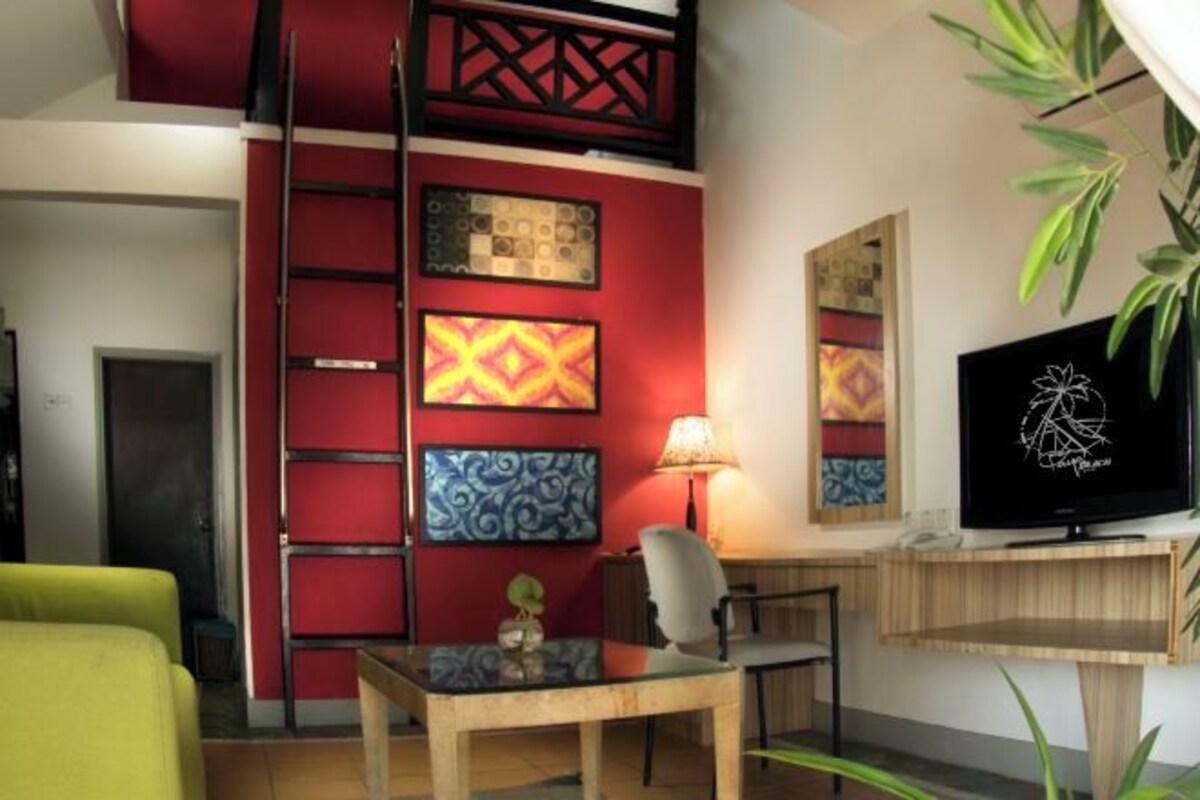 A modern living room with a red accent wall, a glass coffee table, a TV, and a plant.