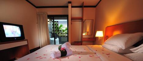 Habitación de hotel con cama, televisión, mesita de noche y balcón con vistas a palmeras.