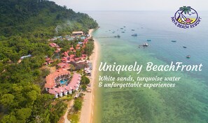 An aerial view of a beach resort with a clear beach, turquoise water, and a dense forested area. - Paya Beach Spa & Dive Resort (Tioman Island)