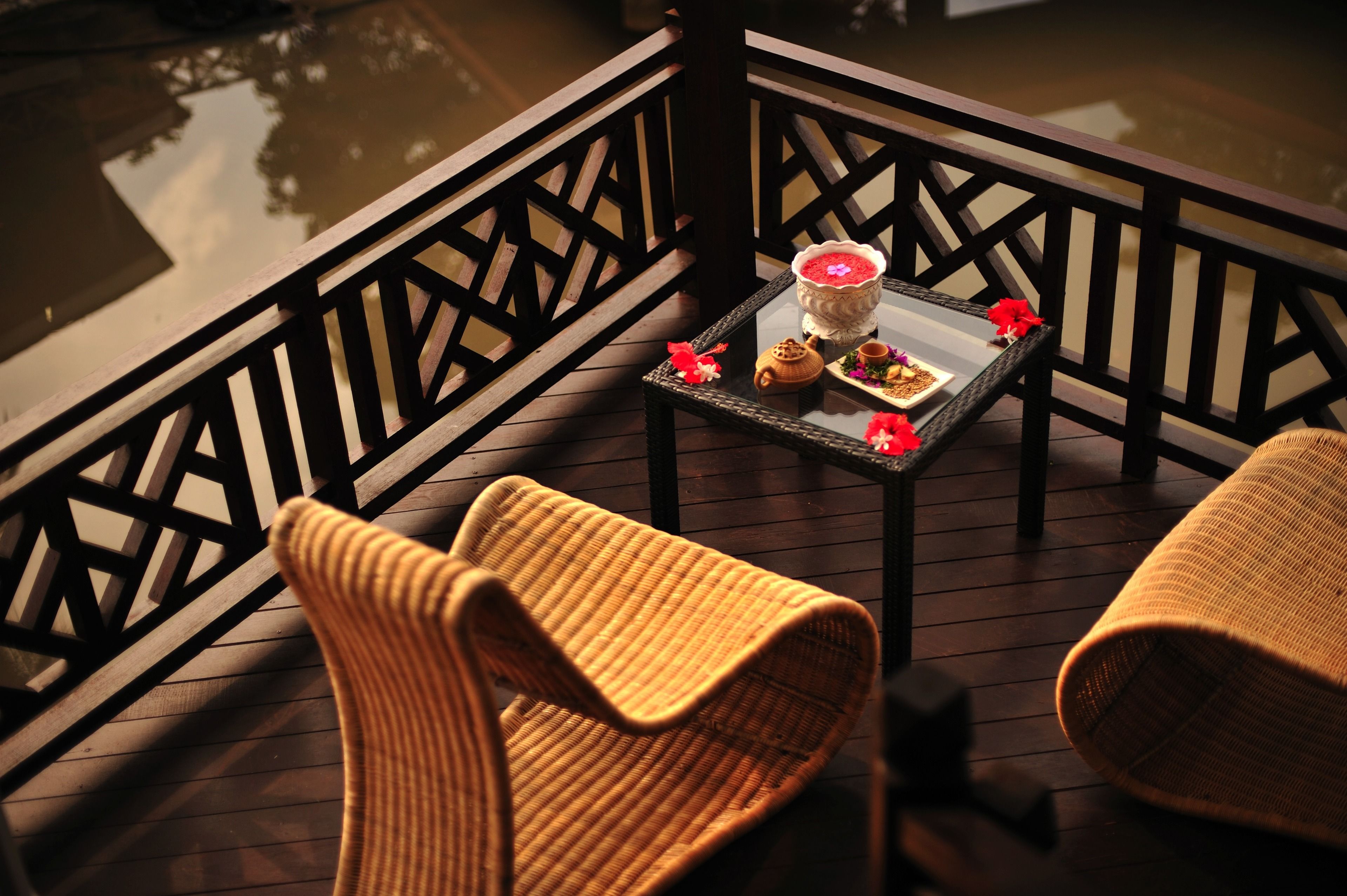 A wooden deck with two wicker chairs and a table with a teapot and cups.