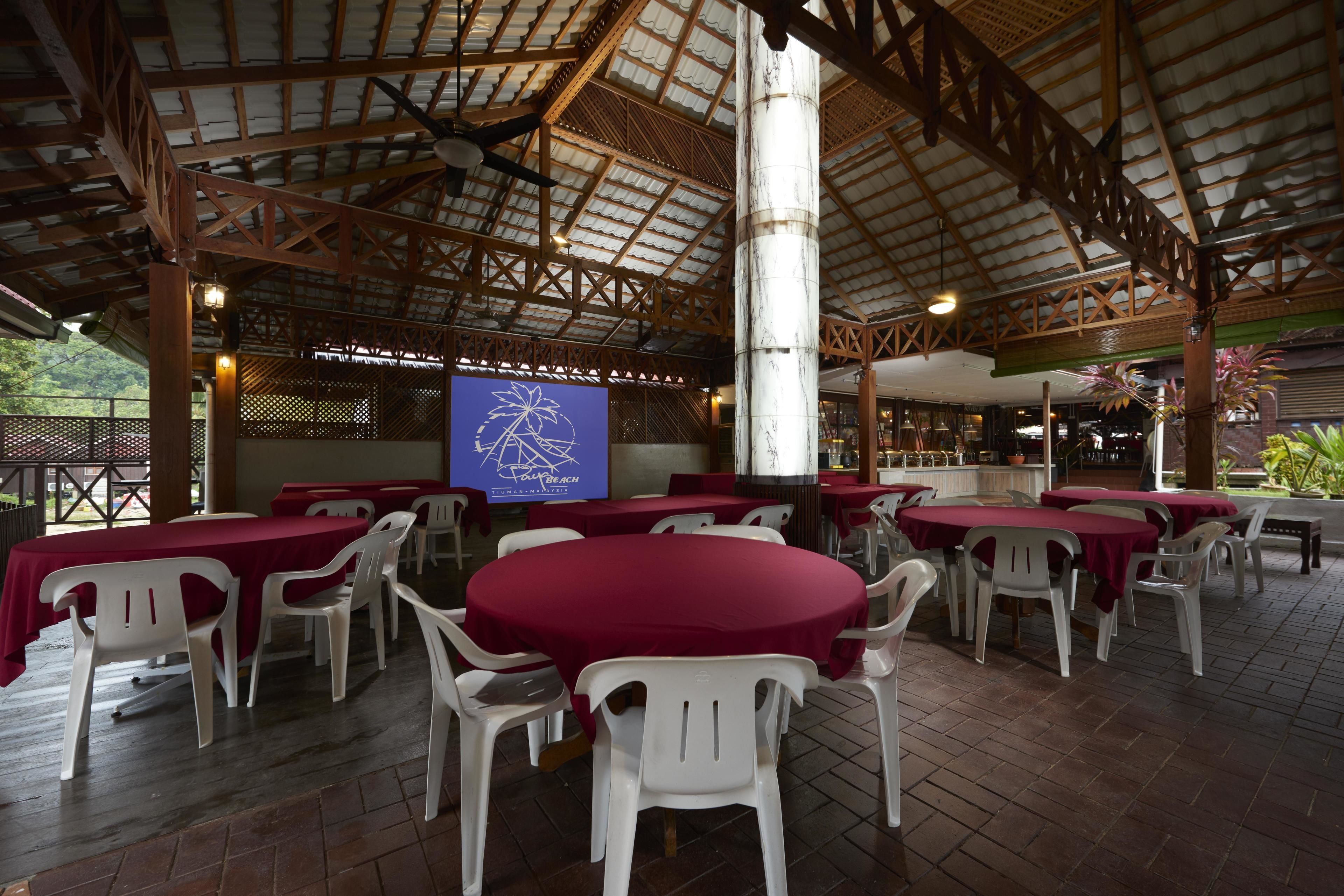 An outdoor dining area with round tables covered in red tablecloths and white plastic chairs.