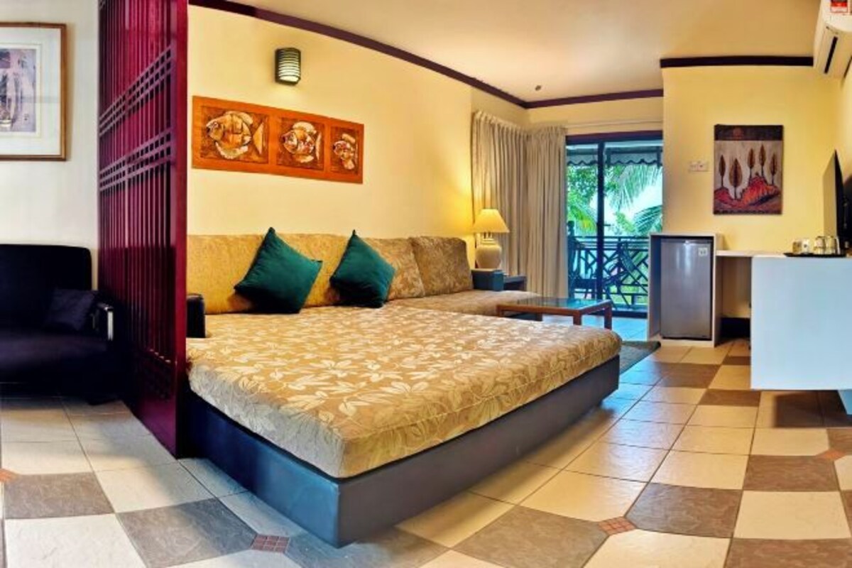 Habitación de hotel con una cama grande, un escritorio, una silla y un balcón con cortinas.