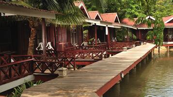 A wooden dock leading to a row of traditional-style buildings with red roofs, surrounded by lush greenery.