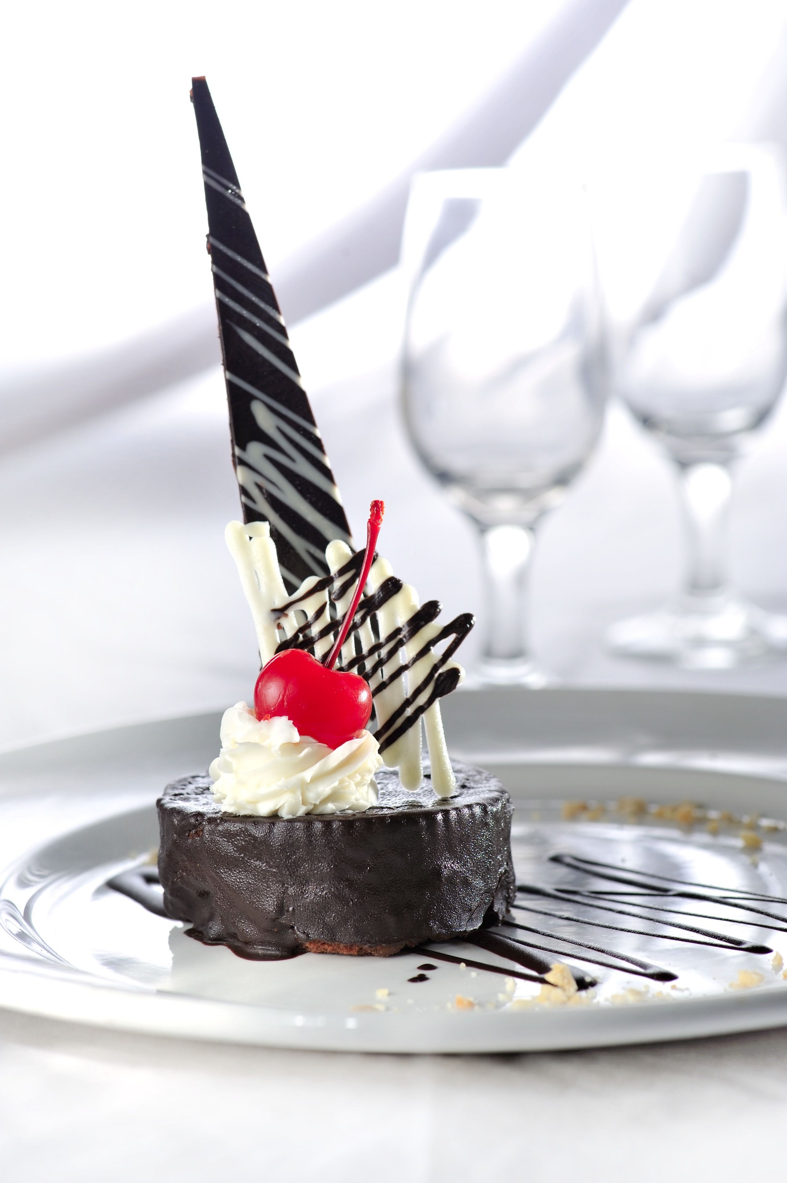 Ein Dessert auf einem Teller mit Schokoladestück und Kirsche obenauf.