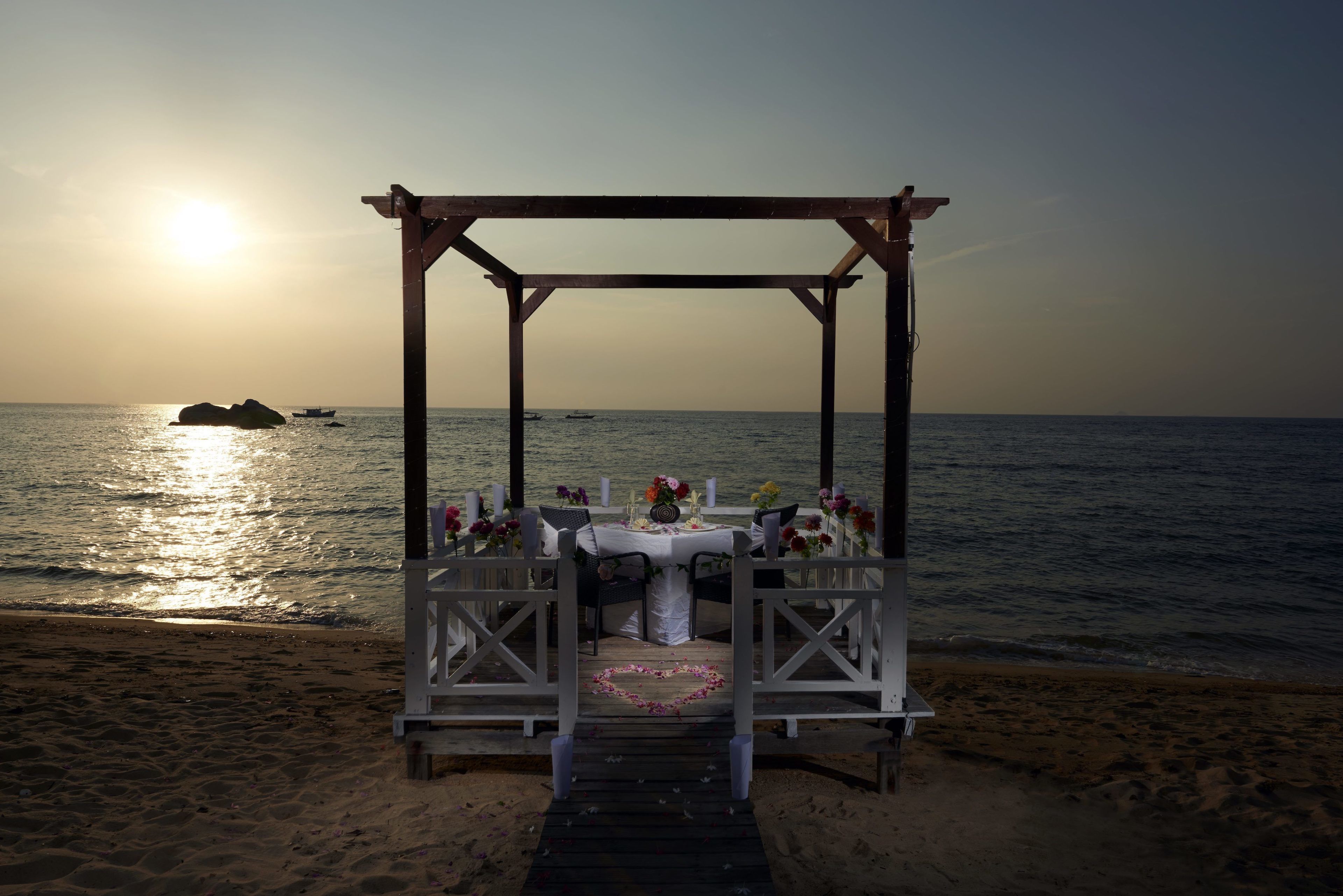 Een prieeltje aan het strand, met een tafel gedekt voor twee personen, met uitzicht op zee.