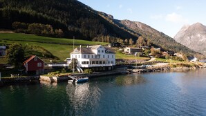 A lakeside property with a large white house, a red barn, and a boat docked near the shore. - Fjærland Fjordstove Hotell (Sogndal)