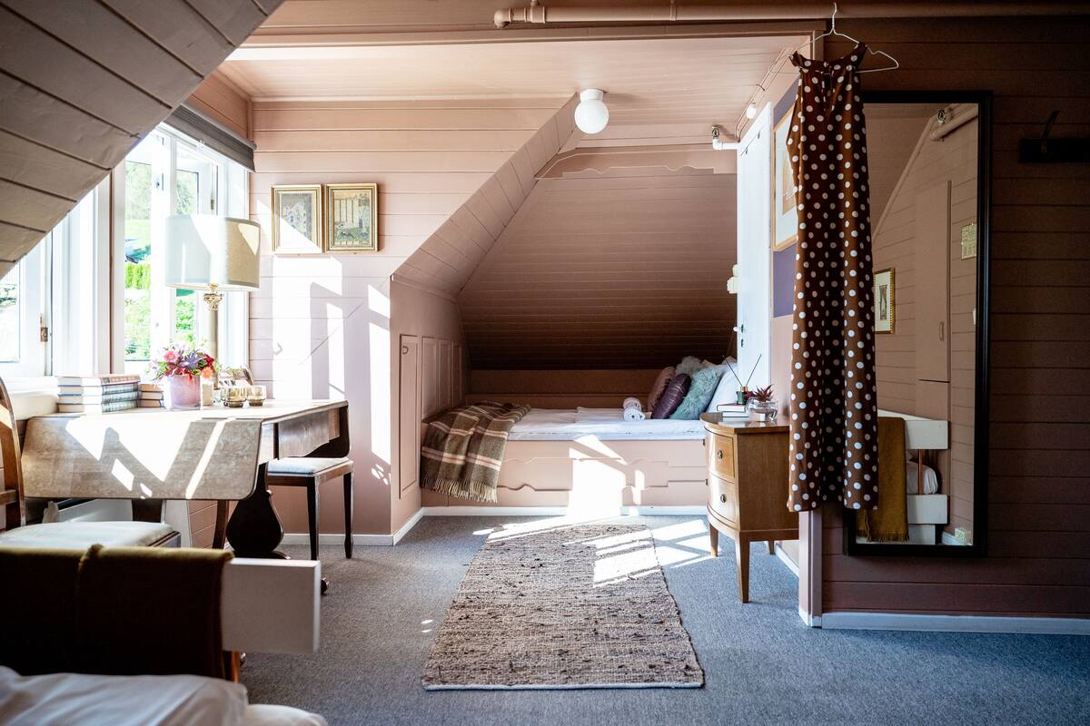 Ein gemütliches Schlafzimmer im Dachgeschoss mit schrägen Wänden, einem Bett, einem Schreibtisch und einer Kommode.