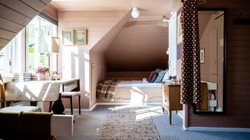Un dormitorio acogedor en el ático, con techo inclinado, cama, escritorio y cómoda.