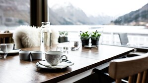 A table with a cup, saucer, and small cups, with a view of mountains through a window. - Fjærland Fjordstove Hotell (Sogndal)