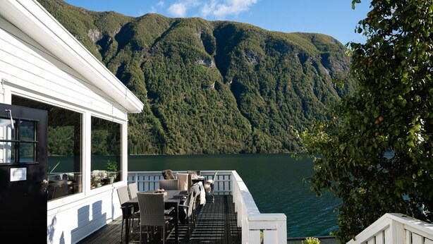 A deck with outdoor seating overlooking a lake and forested mountains. - Fjærland Fjordstove Hotell (Sogndal)