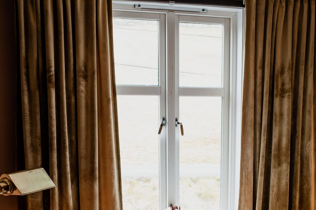 Ein gemütliches Zimmer mit einem Bett, einem Sessel und einem fenster mit Vorhängen.