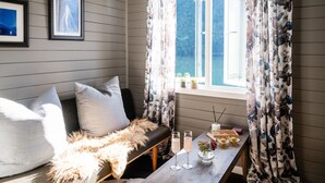 A cozy room with a sofa, a table with drinks, and a window with curtains. - Fjærland Fjordstove Hotell (Sogndal)