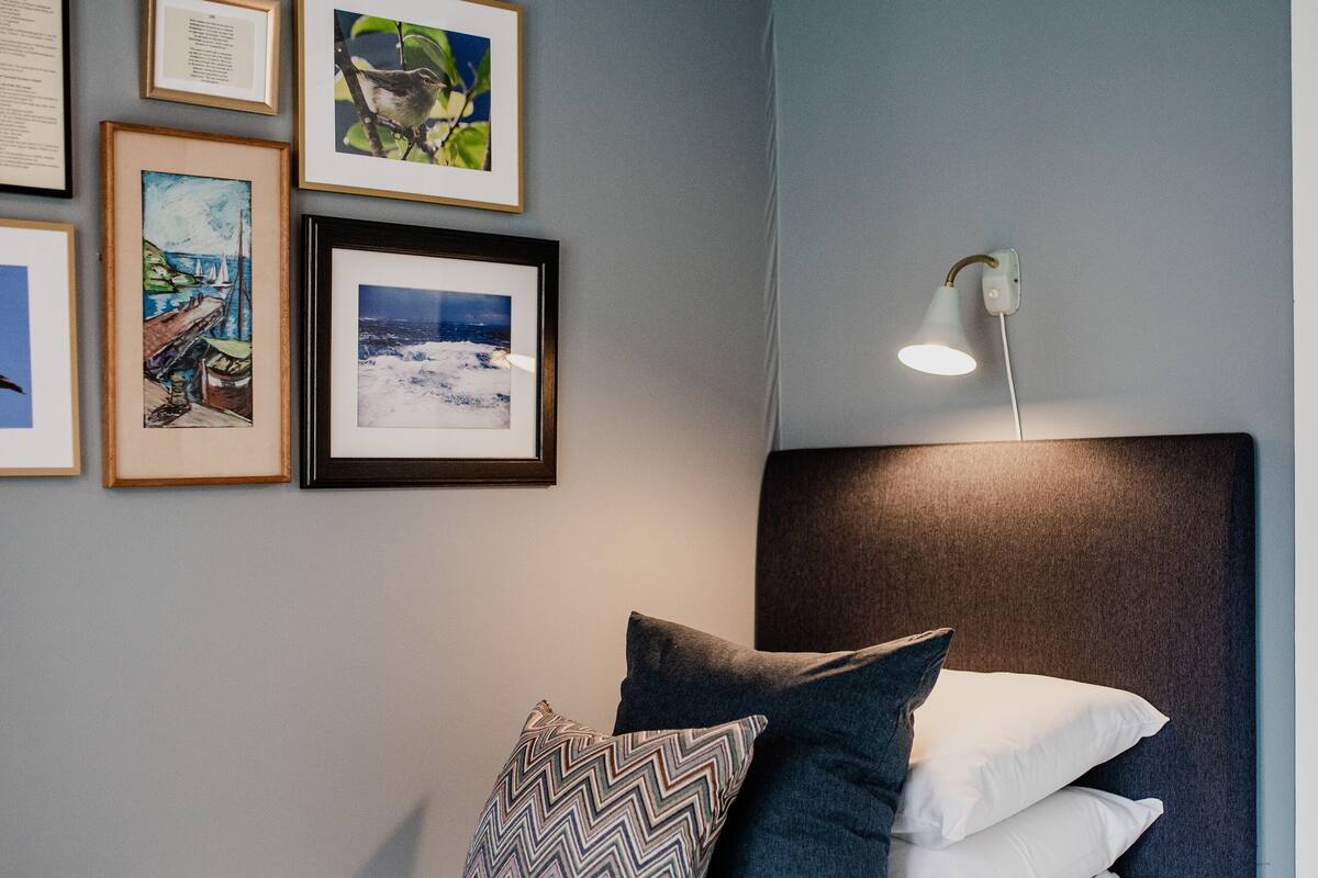 Ein ordentlich eingerichtetes Schlafzimmer mit einem Bett, Kissen und gerahmten Bildern an der Wand.