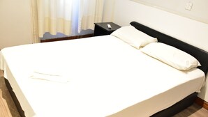 A neatly made bed with white linens, a black headboard, and a bedside table with a remote control. - Zorbas Hotel - Hostel (Athens)