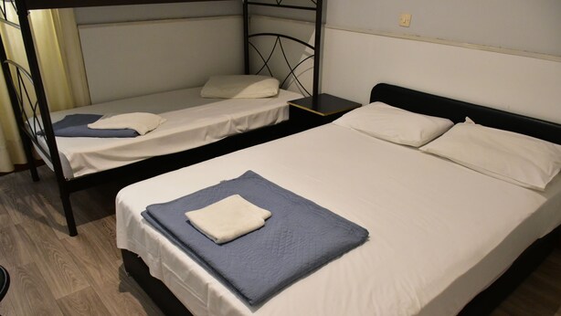 Habitación con dos camas individuales y una cama doble, todas con sábanas y almohadas blancas.