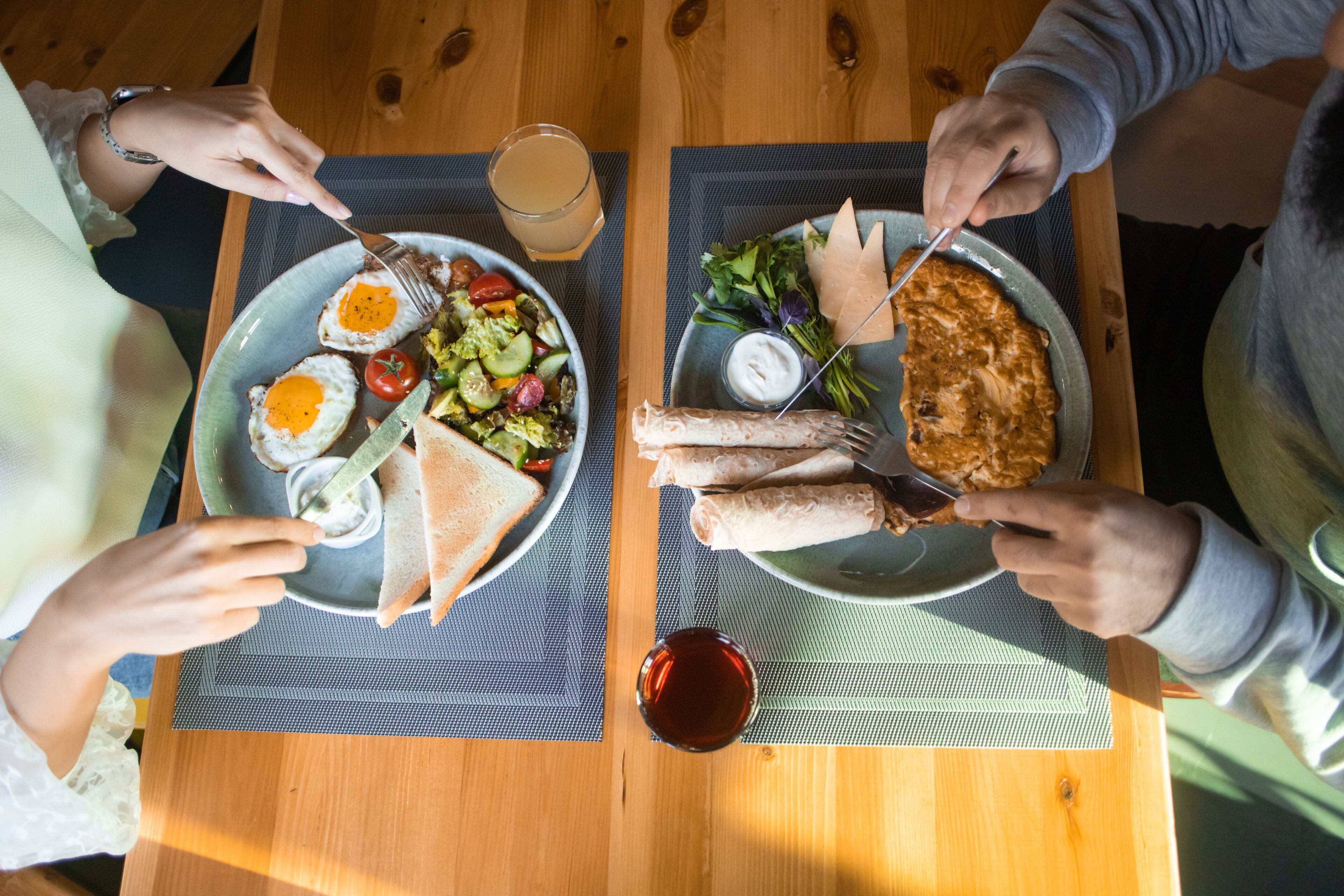 Una mesa de madera con dos platos de comida, un vaso de jugo y un tazón pequeño de salsa.