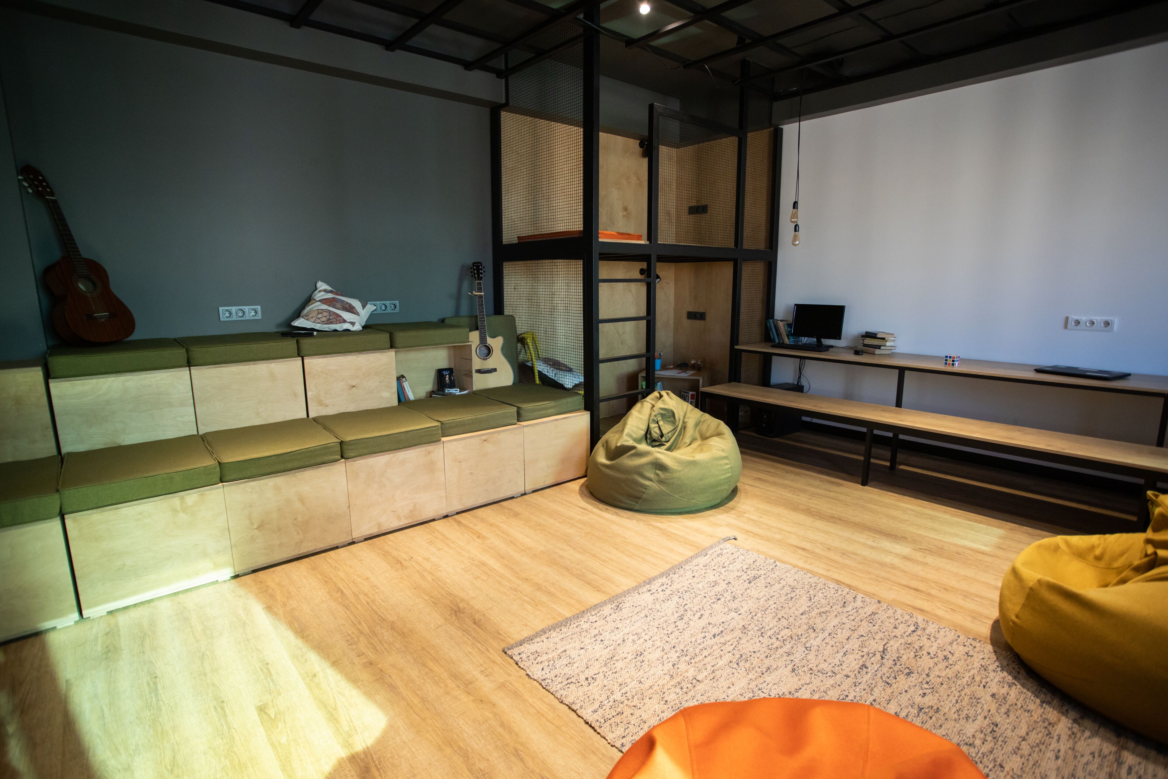 A modern, well-lit room with a wooden floor, a green sofa, a yellow bean bag, a small rug, and a guitar against the wall.