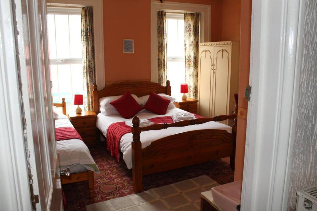 A bedroom with a wooden bed, two bedside tables, a wardrobe, and a window with curtains.