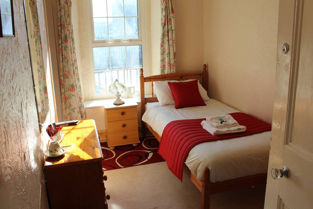 A bedroom with a wooden bed, a bedside table, a nightstand, and a window with floral curtains.