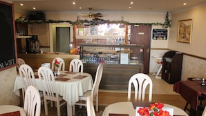 A restaurant interior with white tables, chairs, a counter with a display case, and a menu stand. - The Middlegate Hotel (Pembroke)
