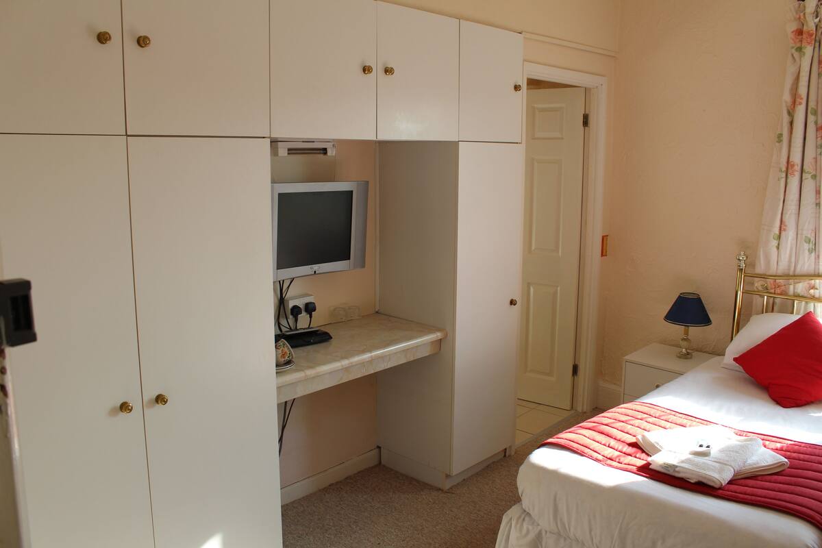 A bedroom with a bed, a desk with a computer, and a wardrobe.