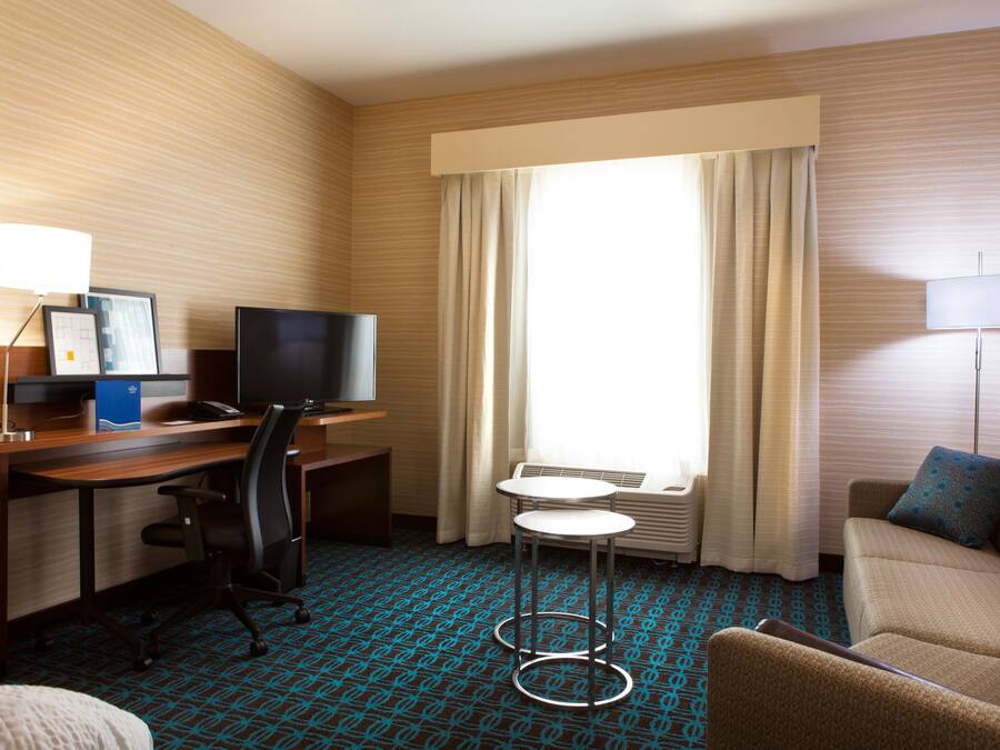 A hotel room with a desk, a television, a chair, a sofa, and a window with curtains.