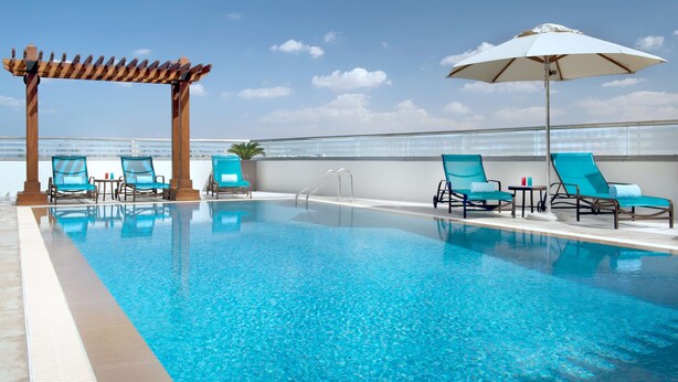 Una piscina en la azotea con agua cristalina, rodeada de sillones de descanso y una pérgola.