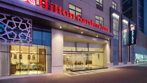 Exterior de un hotel Hilton Garden Inn con fachada moderna, amplias ventanas de vidrio y un llamativo logotipo rojo y blanco.