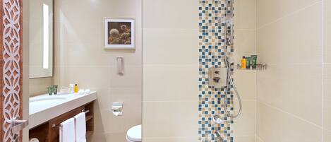 Un baño moderno con bañera, ducha e inodoro. Hay un tocador con espejo y un perchero. Un cuadro enmarcado cuelga de la pared sobre el inodoro.