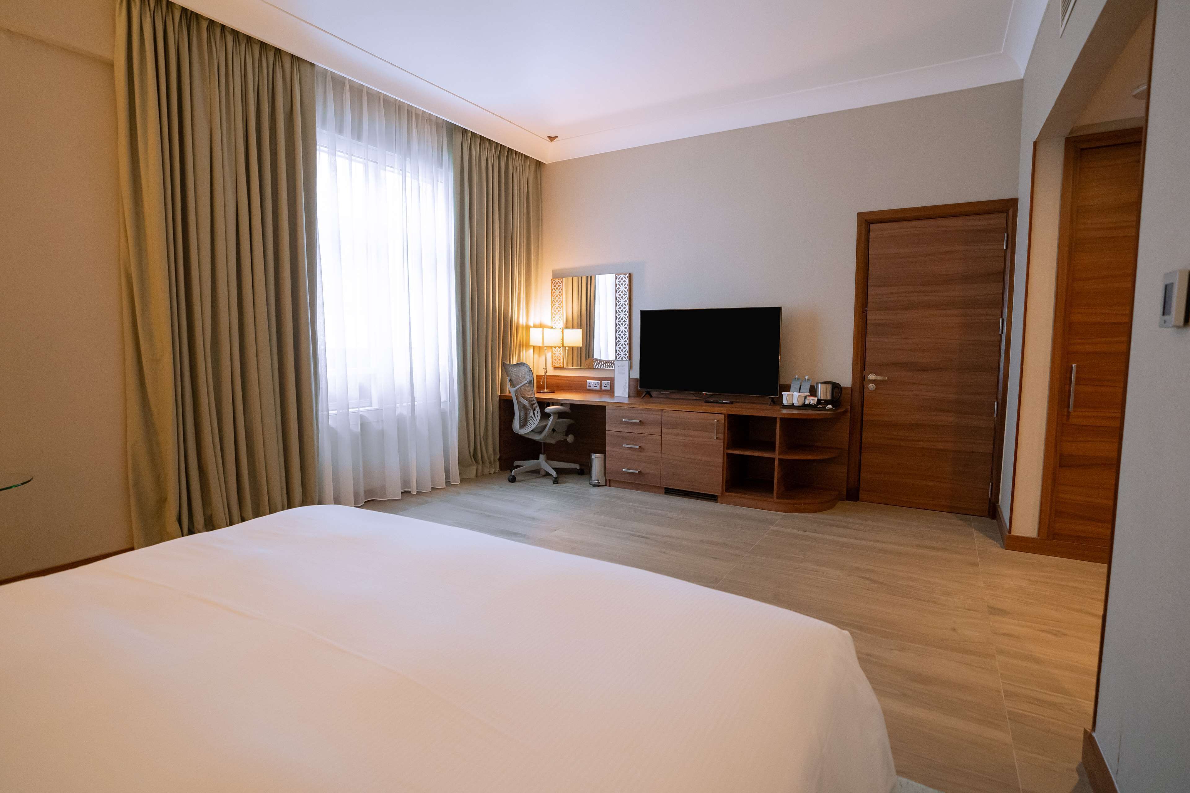 Habitación de hotel con una cama grande, un escritorio con televisor, una silla y un armario de madera.