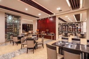 Un moderno vestíbulo de hotel con piso de mármol, una zona de bar central y un área de descanso con mesas y sillas.