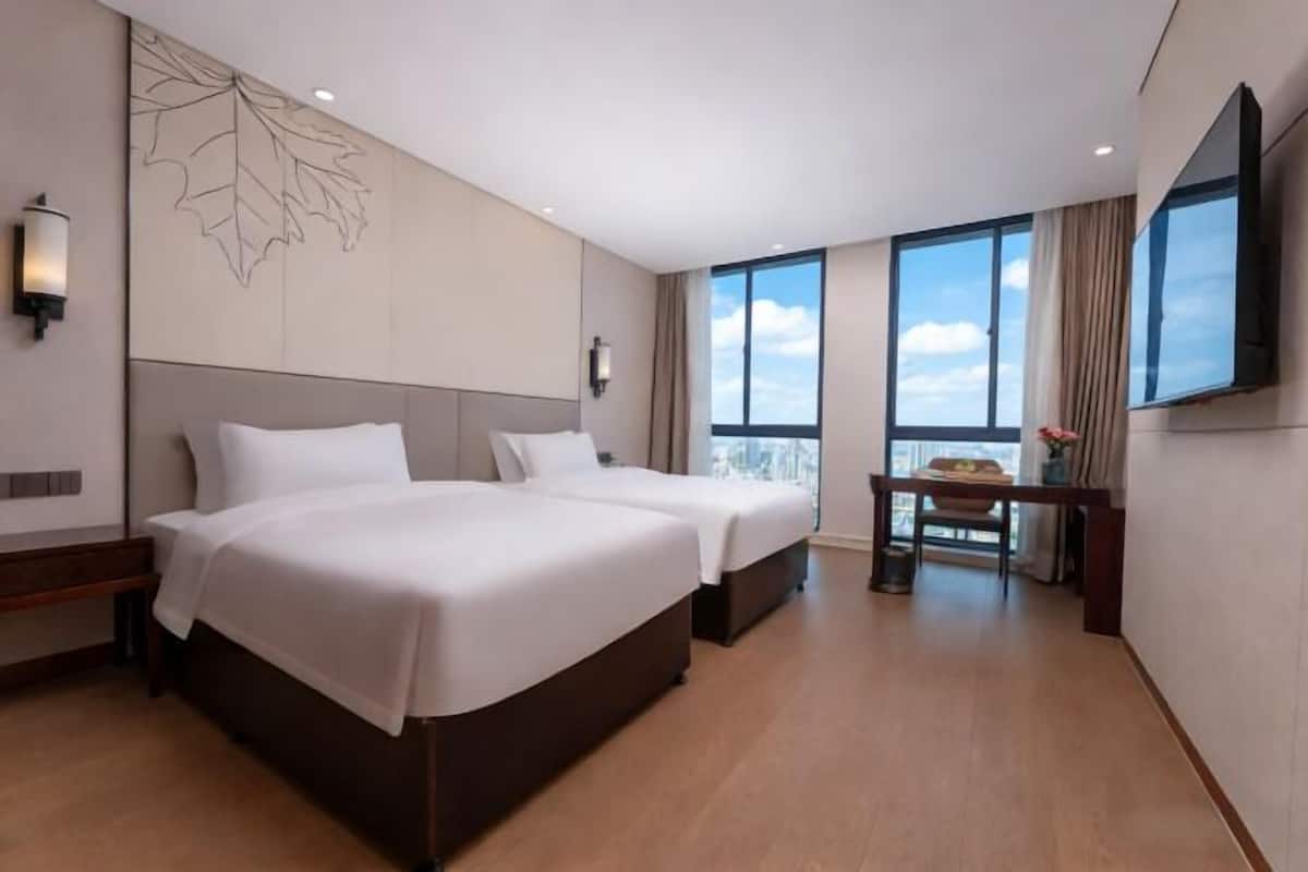 Een hotelkamer met twee bedden, een bureau, een groot raam en een aan de muur bevestigde televisie.