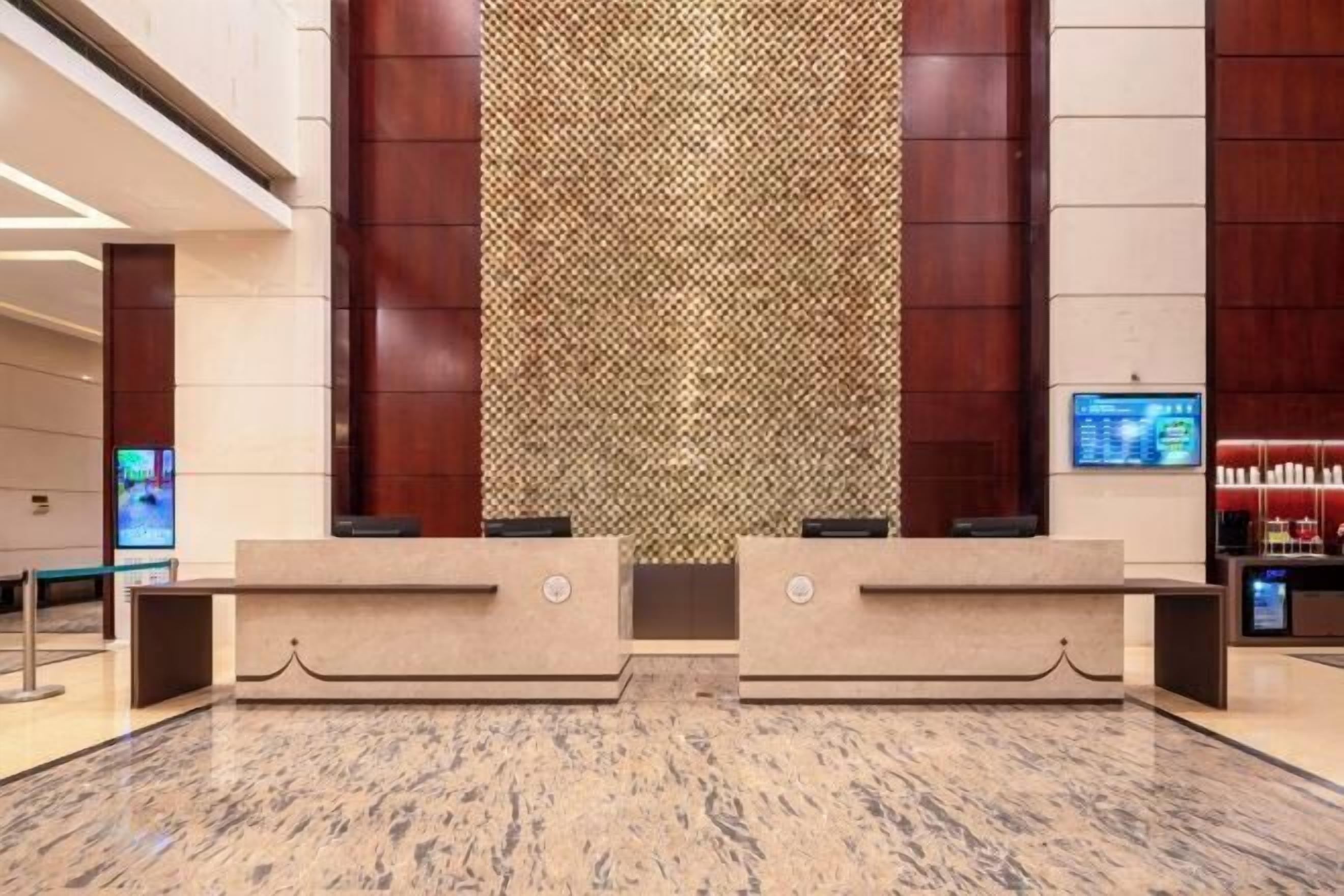 Un área de recepción con suelo de mármol, dos mostradores y una pared con diseño, además de una pantalla digital a la derecha.
