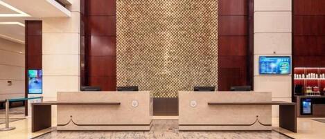 Un área de recepción con suelo de mármol, dos mostradores y una pared con diseño, además de una pantalla digital a la derecha.