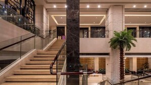 Eine moderne Hotelhalle mit einer zentralen Säule aus Marmor, einer Treppe und einem Palmenbaum.