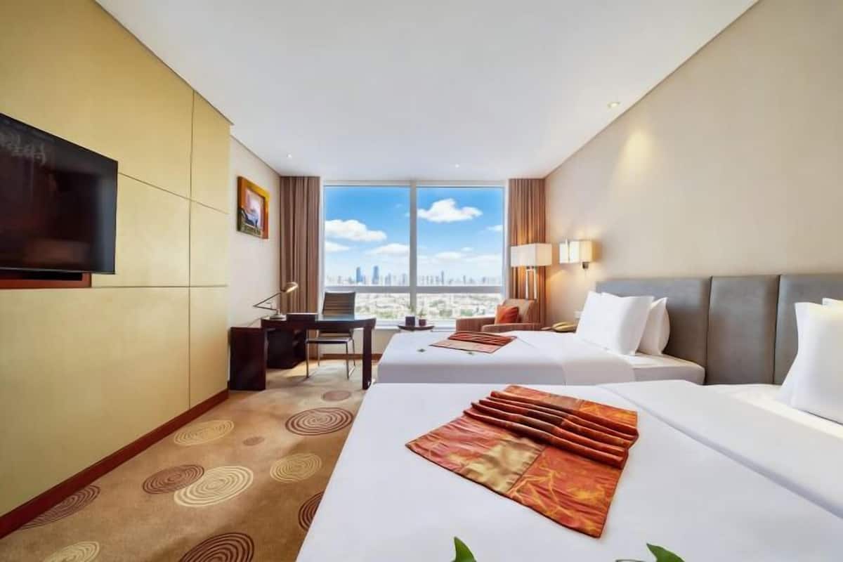 Hotelkamer met twee bedden, een bureau, een televisie en een groot raam met uitzicht op de stad.