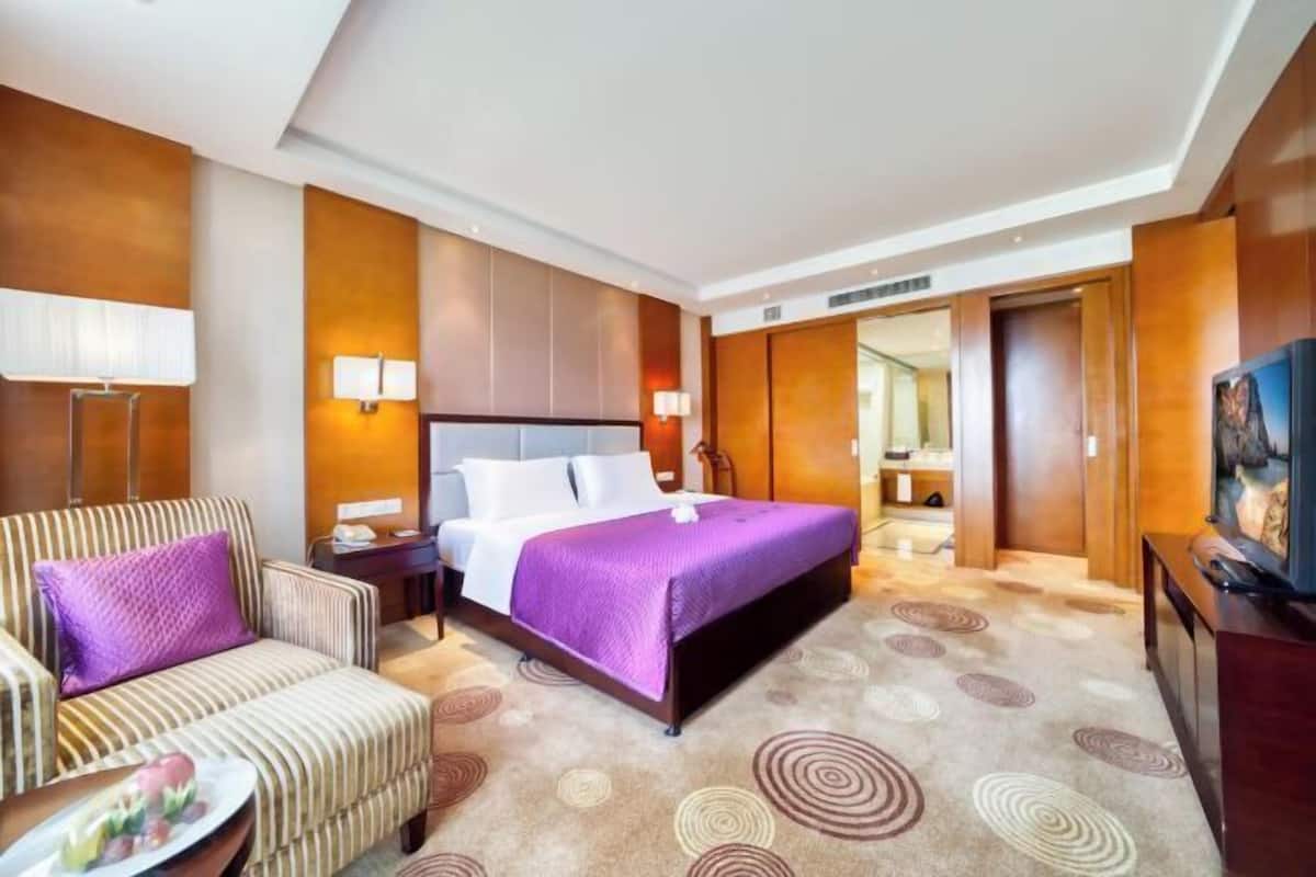 Een hotelkamer met een bed, een bank, een nachtkastje, een lamp en een televisie.
