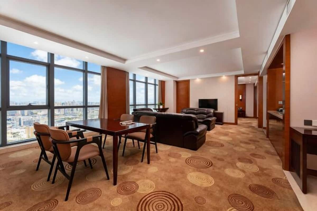 Een moderne hotelkamer met een groot raam, een zithoek met tafel en stoelen, een bank en een flatscreen televisie.