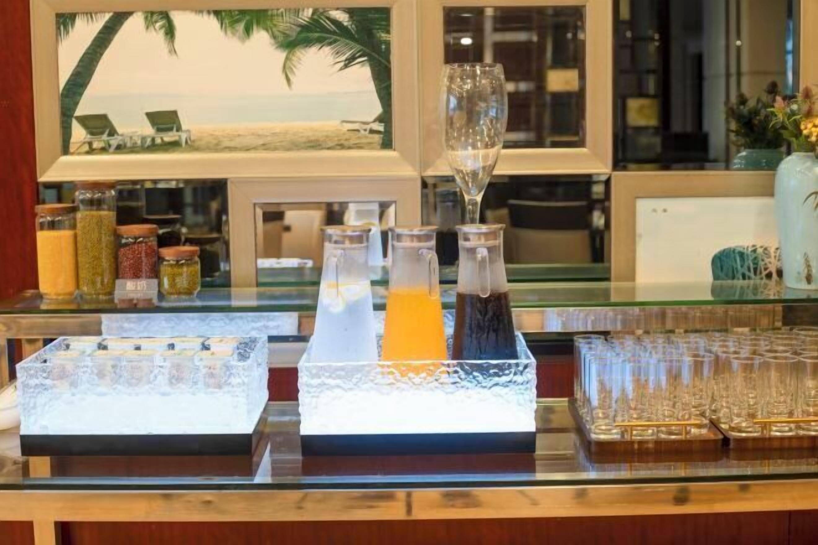 Un bar où l’on peut prendre le petit-déjeuner, avec vue sur une plage tropicale, une variété de condiments et un verre de jus d’orange.